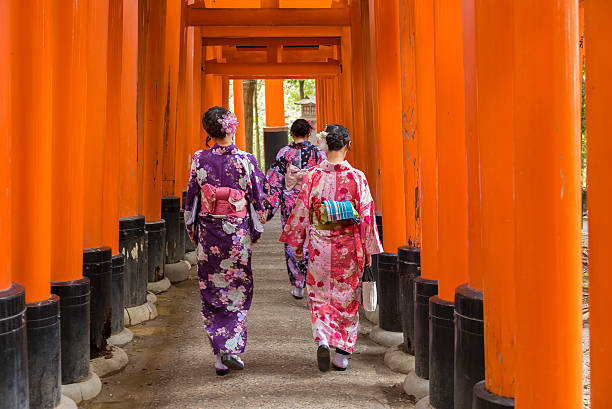 Kyoto, Japan - April 8, 2016: Japanese girls wearing traditional Japanese kimonos, walking through a long series of inscribed Torii gates at Fushimi Inari-Taisha, on the outskirts of the ancient Japanese city of Kyoto.