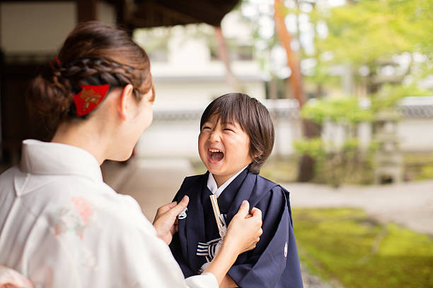 A young Japanese boy and his mother are wearing traditional kimono dress while celebrating shichigosan. He is smiling up at his mother while she straightens his robe. Shichigosan is a coming of age rite for 5 year old boys. They are at the Chion-ji Temple in Kyoto Japan.